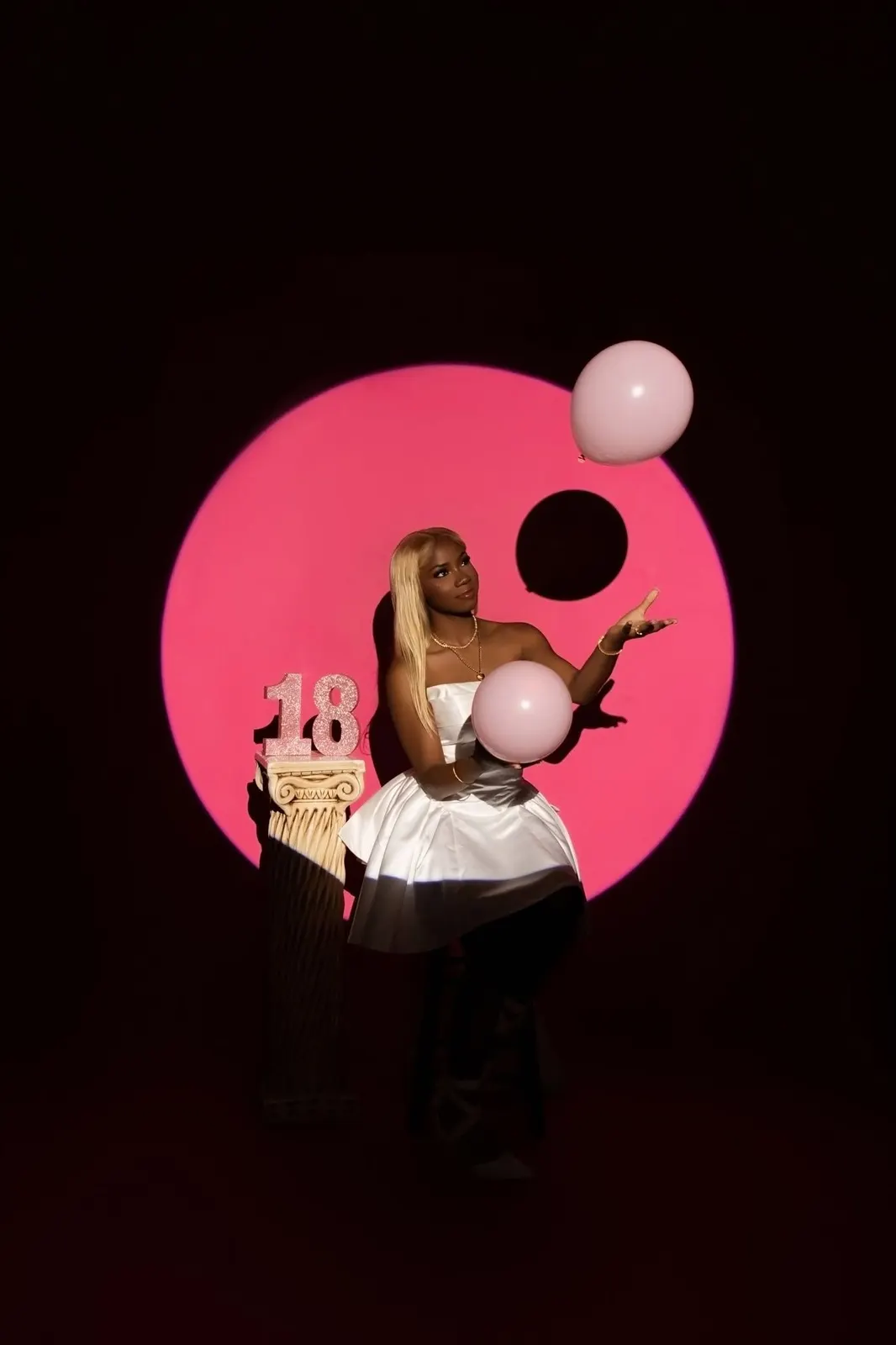 A young woman celebrating her 18th birthday with balloons against a pink circle backdrop