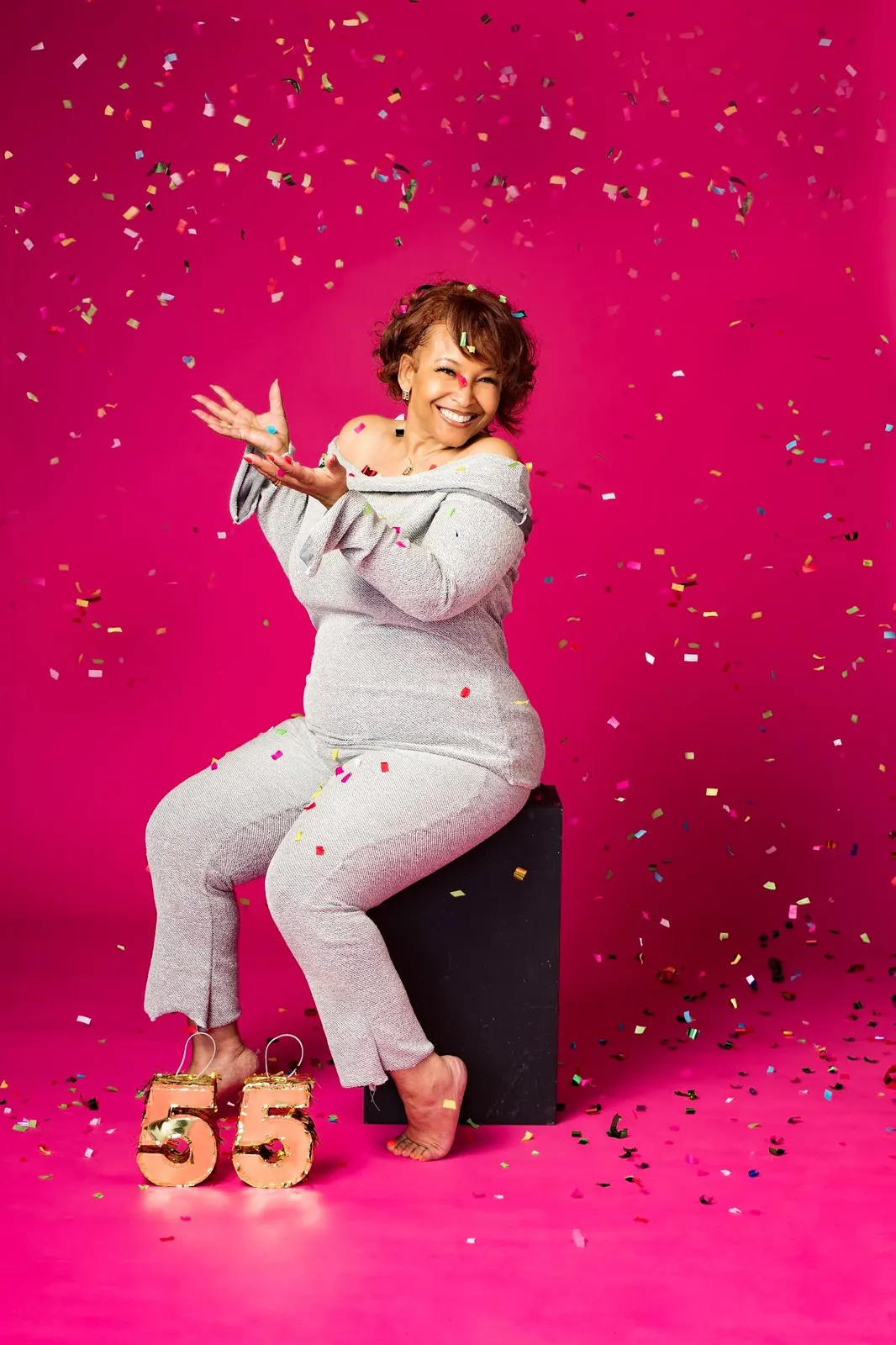 A woman celebrating her 55th birthday with confetti on a hot pink backdrop