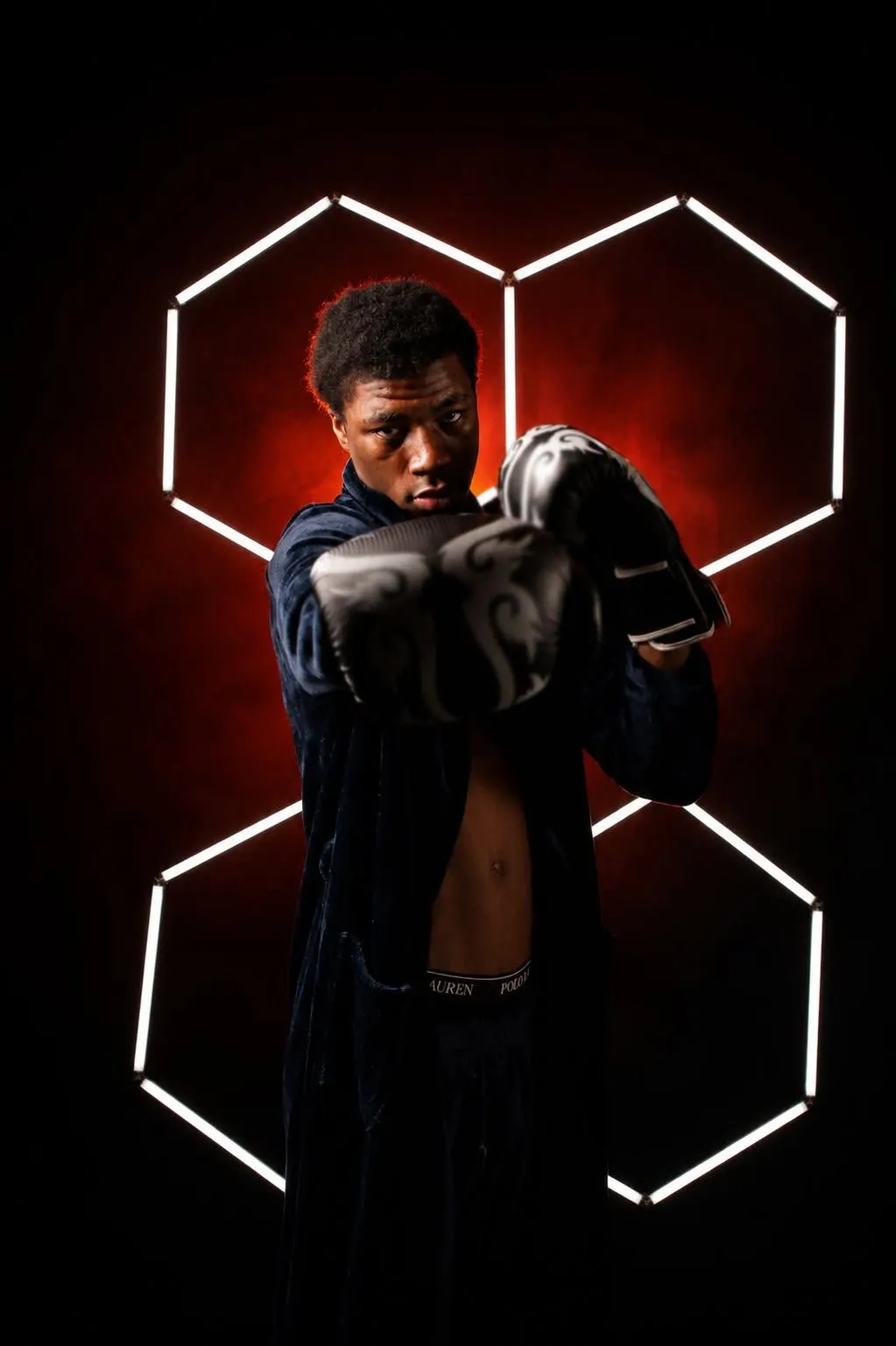 A young boxer raising his gloves in a guard stance under hexagon lights