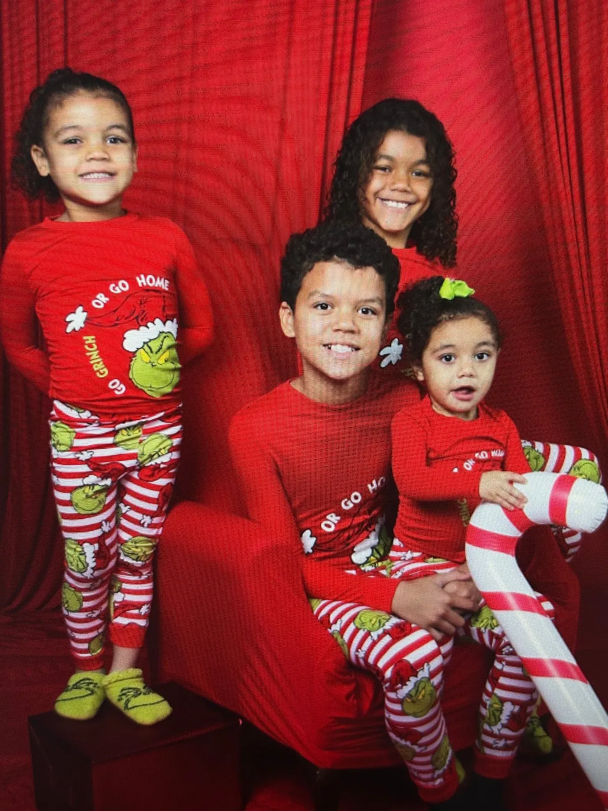 Four siblings in matching red Christmas pajamas on a red studio set