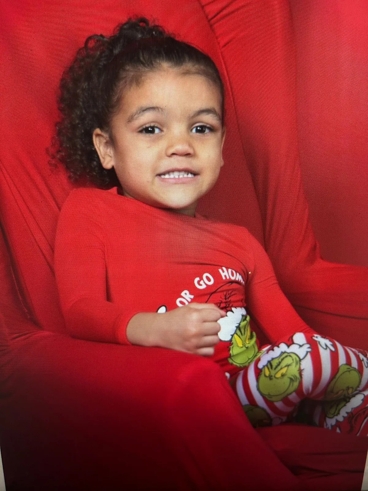 A smiling little girl in Christmas pajamas in a red armchair