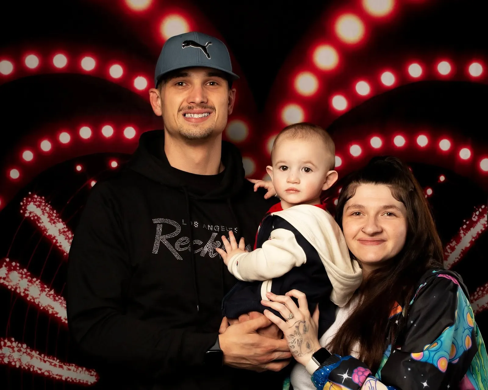 A couple holding their baby in front of red marquee lights