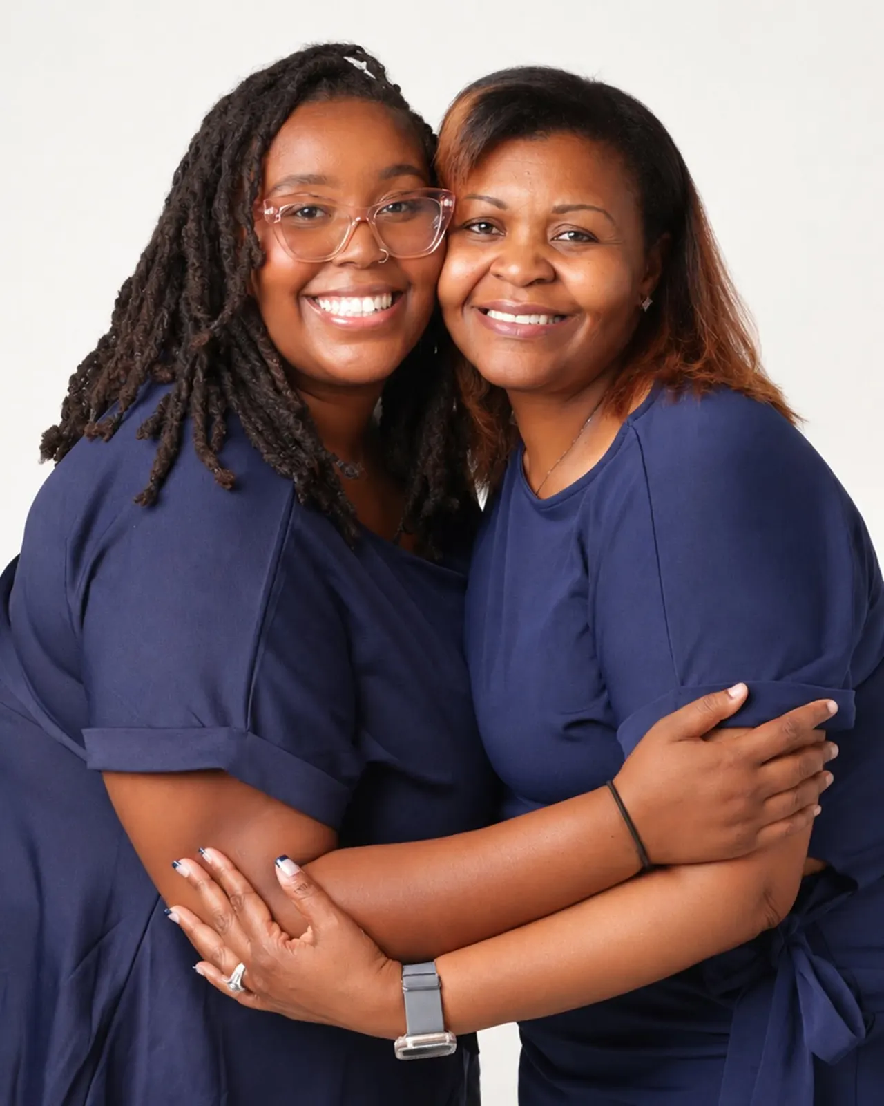 A mother and daughter in navy embracing cheek to cheek on a white backdrop