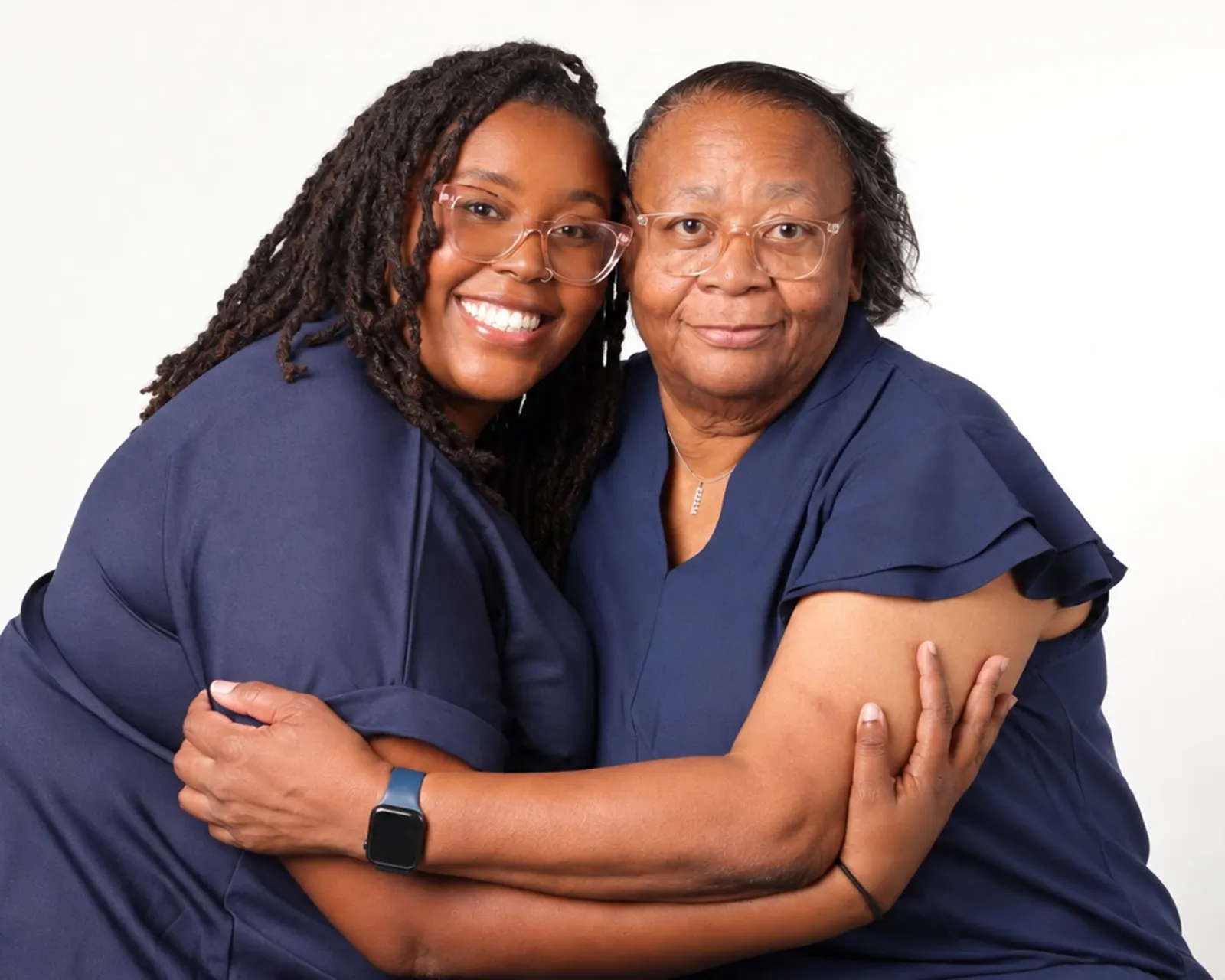 Three generations of women in navy hugging and smiling on a white backdrop